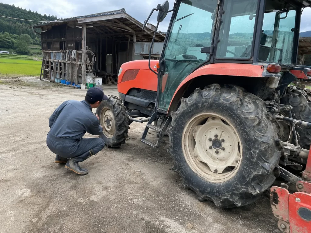 走行前にトラクターのタイヤまわりを確認する作業者